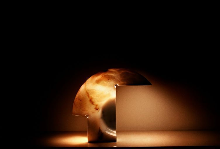 Una sfera dorata luminosa, parzialmente nascosta dietro un blocco beige su uno sfondo scuro.