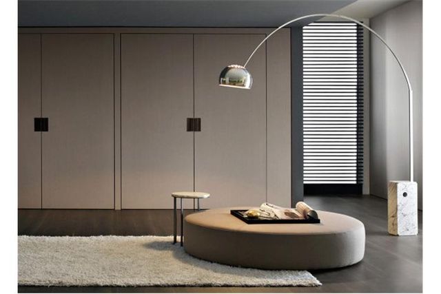 Soggiorno moderno e minimalista con divano rotondo marrone, lampada da terra ad arco e pensili a muro.