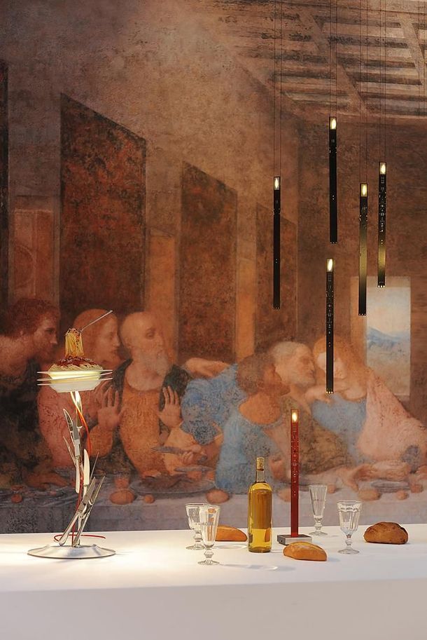 Scena di una cena a lume di candela con persone sedute dietro un tavolo bianco apparecchiato con bicchieri, bottiglie e candele.