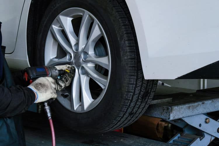 A man is changing a tire on a car with a wrench. | Silvhorn Automotive