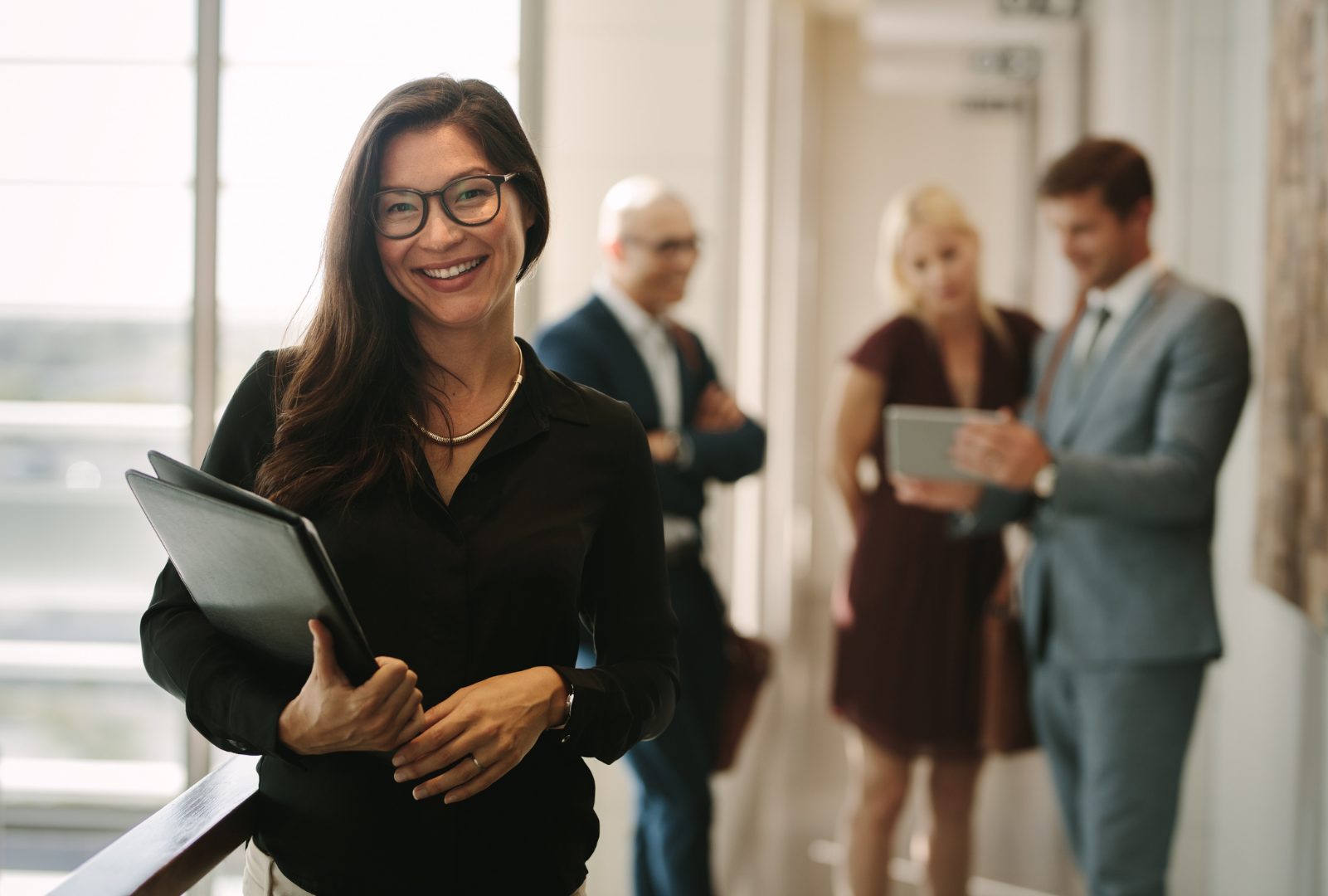 A woman is holding a clipboard in front of a group of business people.