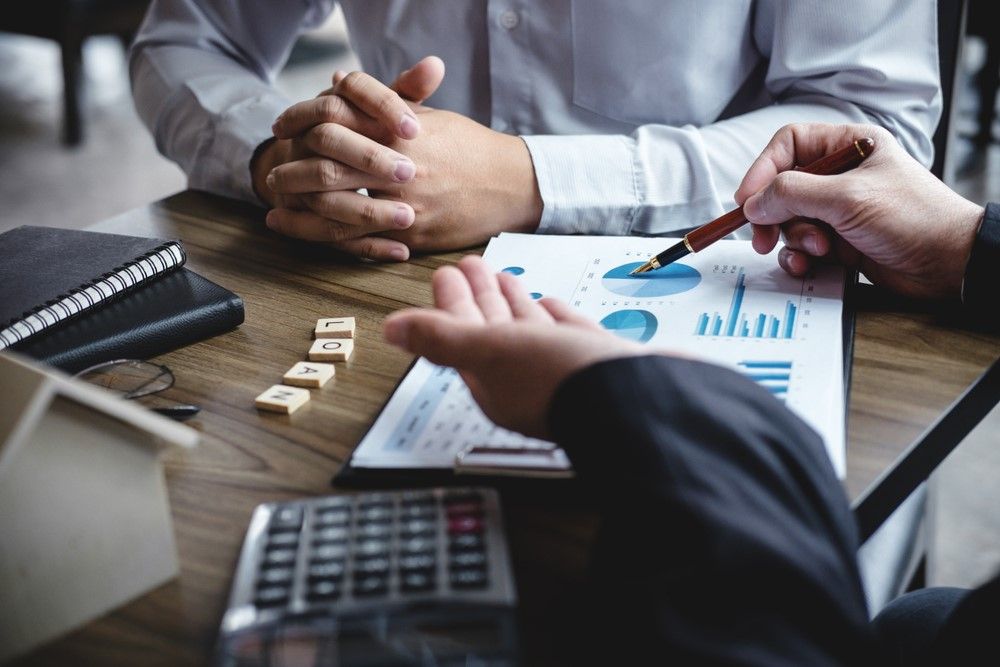 Two Men Are Sitting at a Table Looking at a Graph — Optimus 1 Insurance Brokers in Westcourt, QLD