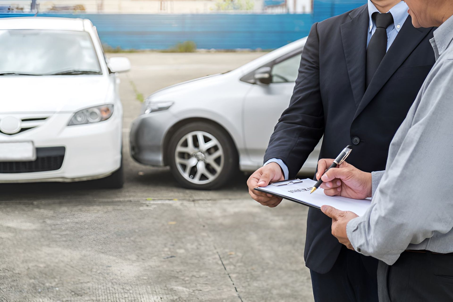 A Man in a Suit is Holding a Clipboard in Front of Two Cars — Optimus 1 Insurance Brokers in Westcourt, QLD