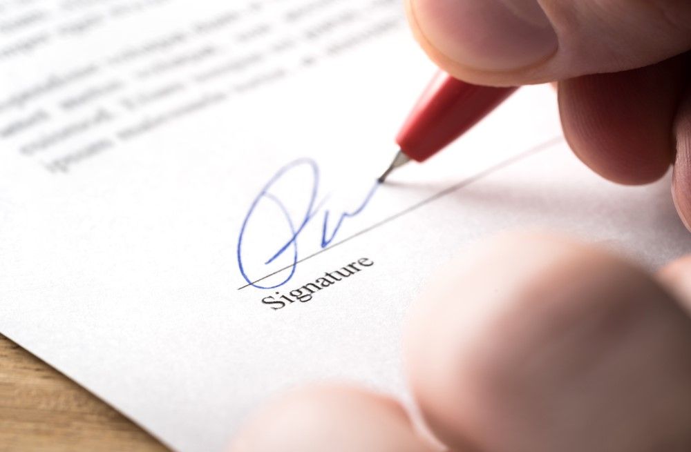 A Person is Signing a Document With a Pen — Optimus 1 Insurance Brokers in Westcourt, QLD