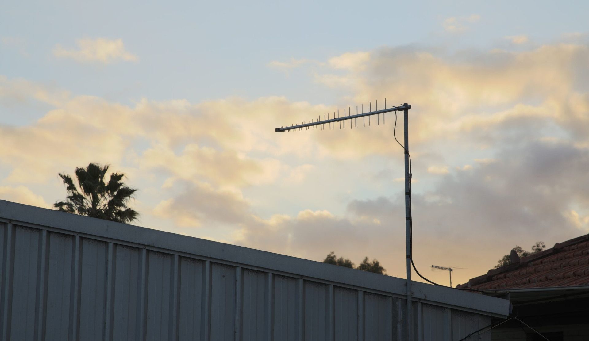 TV antenna on a rooftop with a cloudy sunset background.