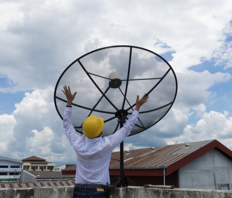 A Man In A Yellow Hard Hat Is Standing In Front Of A Large Satellite Dish — Capricorn Communications in Biloela, QLD