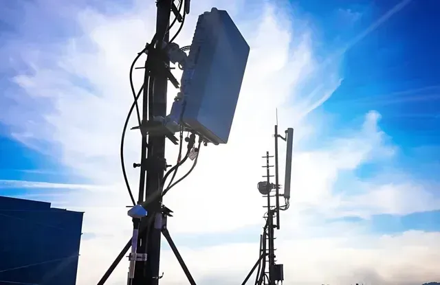 Two communication towers with antennas against a bright blue sky with clouds.