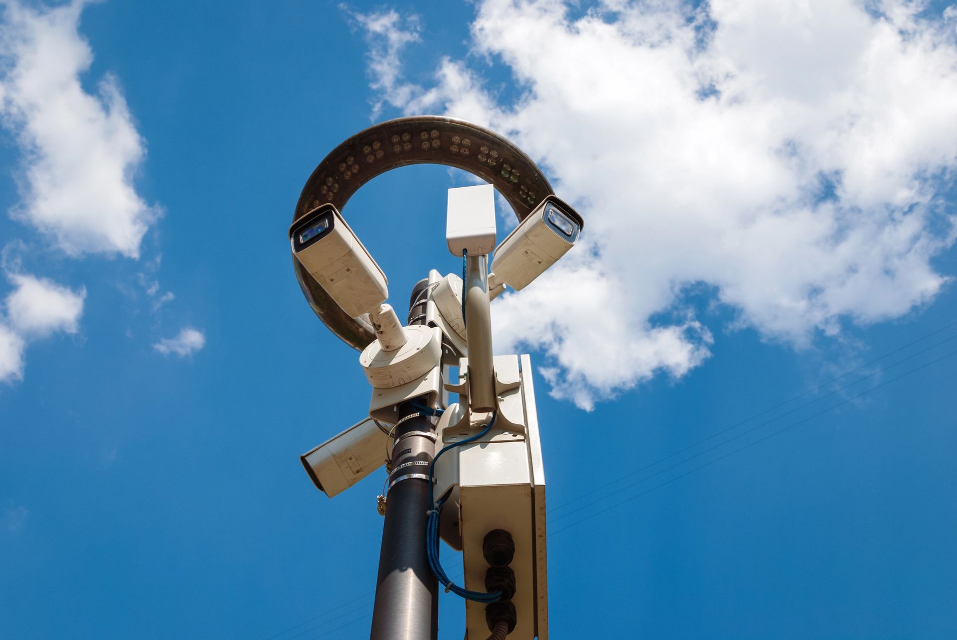 A mobile surveillance unit with cameras mounted on a pole against a blue sky with clouds.