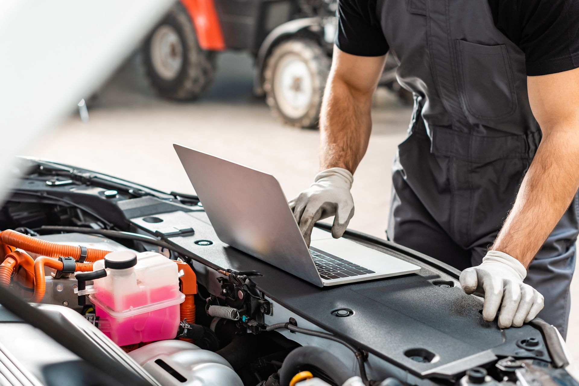 A man is using a laptop computer to work on the engine of a car.