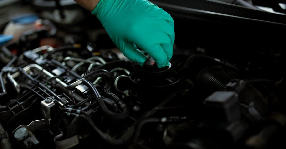 A person wearing green gloves is working on a car engine.