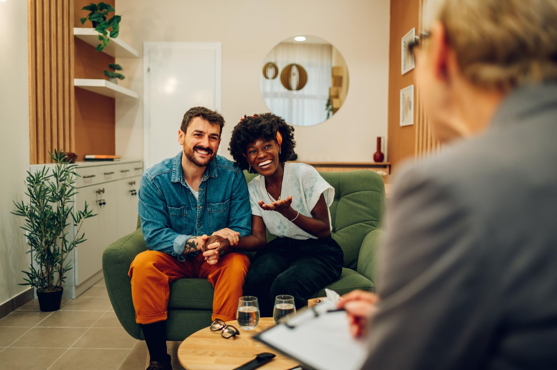 Couple on green couch smiling during a therapy session; counselor with clipboard.