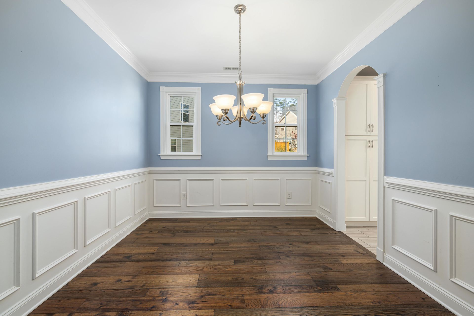 An empty dining room with blue walls and white trim and a chandelier.