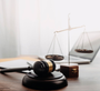Gavel and scales of justice on a desk, with a laptop in the background, symbolizing law and legal proceedings.
