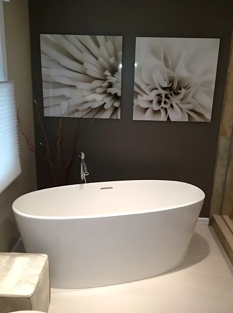 White oval bathtub in a modern bathroom with floral art on a dark gray wall.