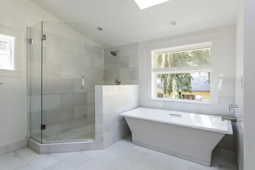 Modern white bathroom with a glass shower, soaking tub, and window.