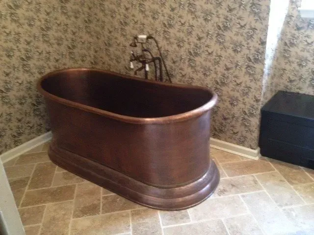 Copper bathtub in a bathroom with patterned wallpaper and tiled floor.