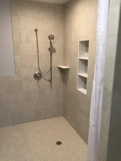 A tiled shower with a built-in shelving unit, shower head, and a white shower curtain.