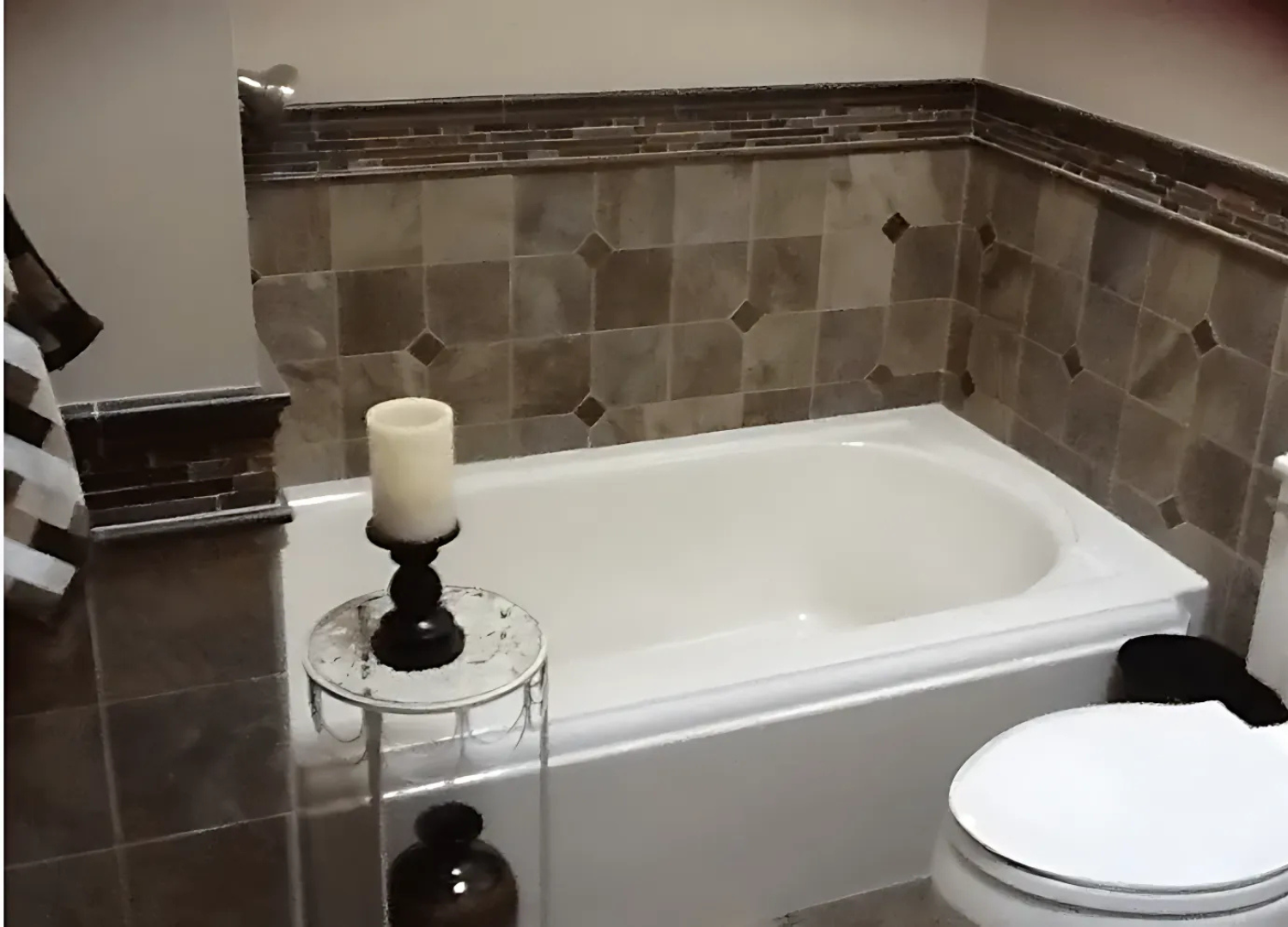 Bathtub in a bathroom with decorative tile wall and a candle on a side table.