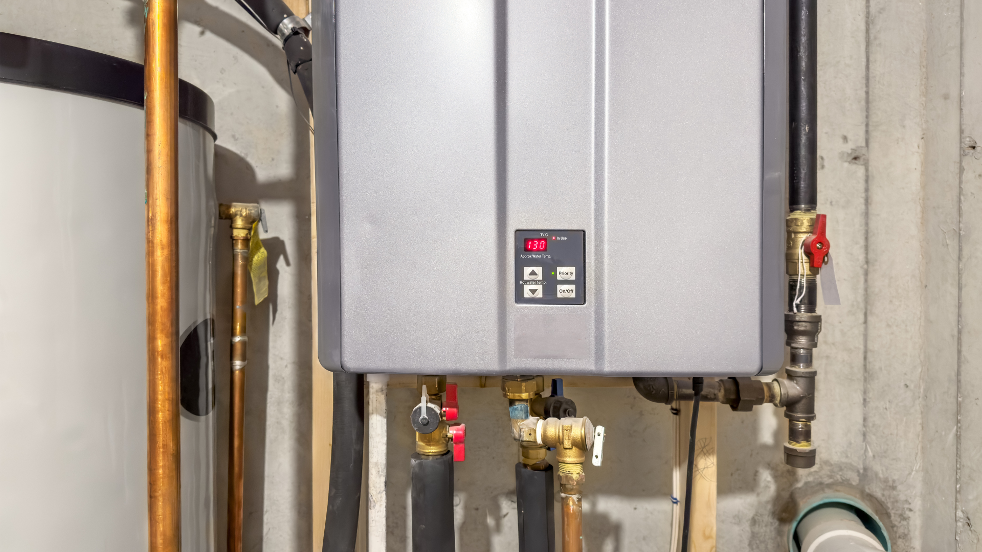 Gray tankless water heater on a concrete wall with connected pipes and a digital display.