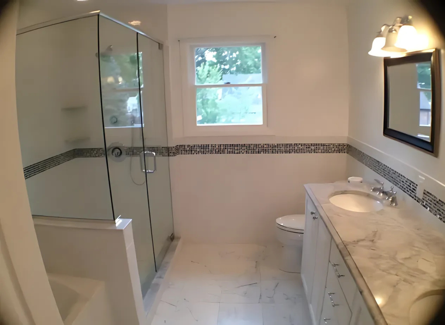 Bathroom with glass shower, white tile walls, vanity, toilet, and window.