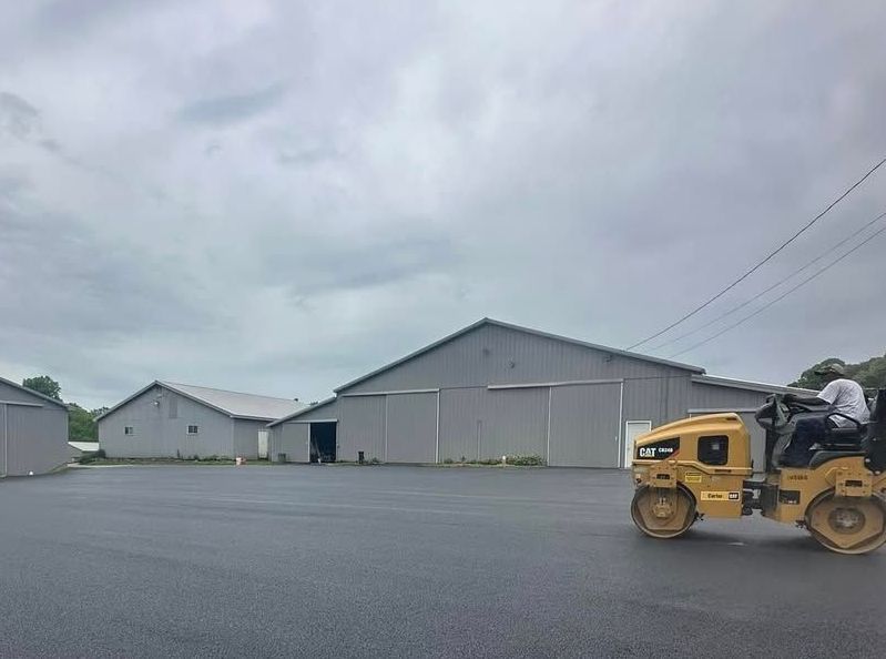 A yellow roller is rolling asphalt in a parking lot in front of a building.