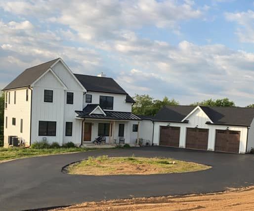 A large white house with a black roof is sitting on top of a dirt hill.
