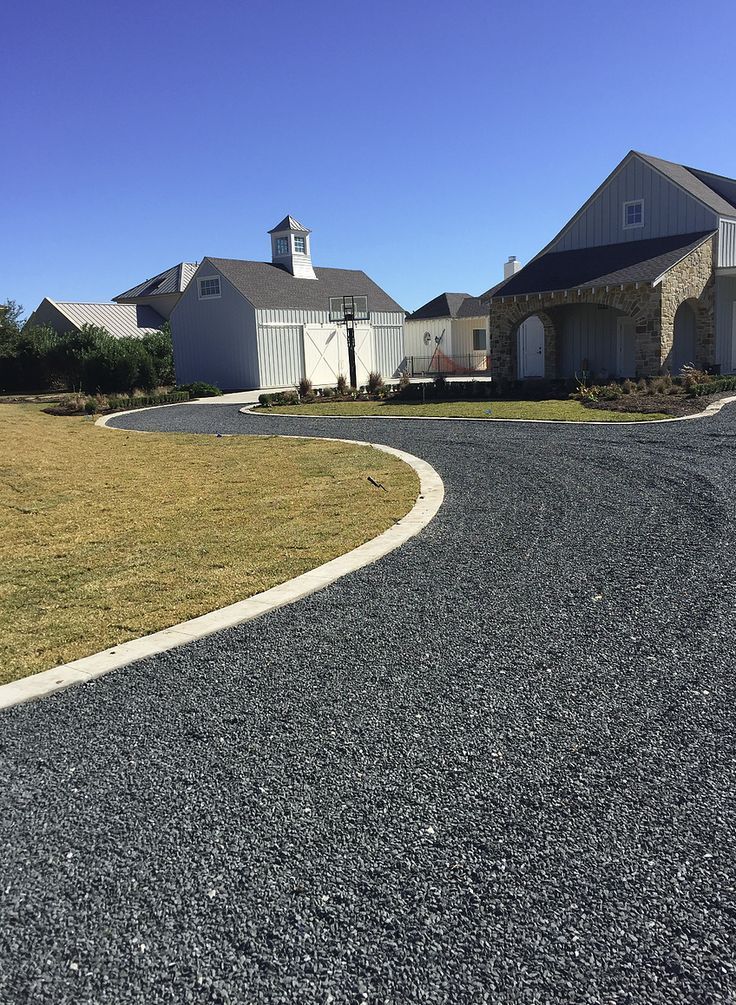 A gravel driveway leading to a large house on a sunny day.