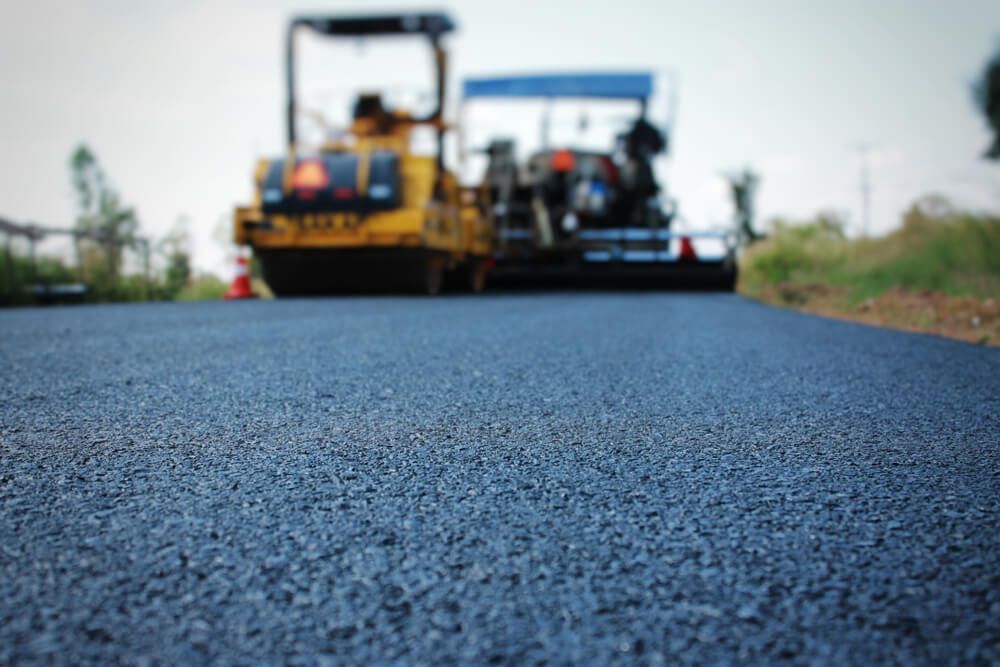 Close-up of freshly paved asphalt road with construction vehicles blurred in background.