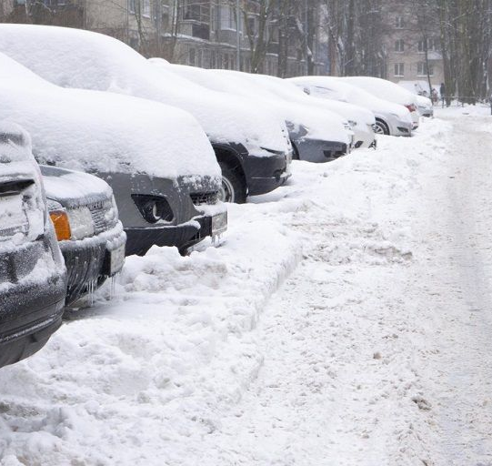 Cars covered in snow parked along a snow-covered road.