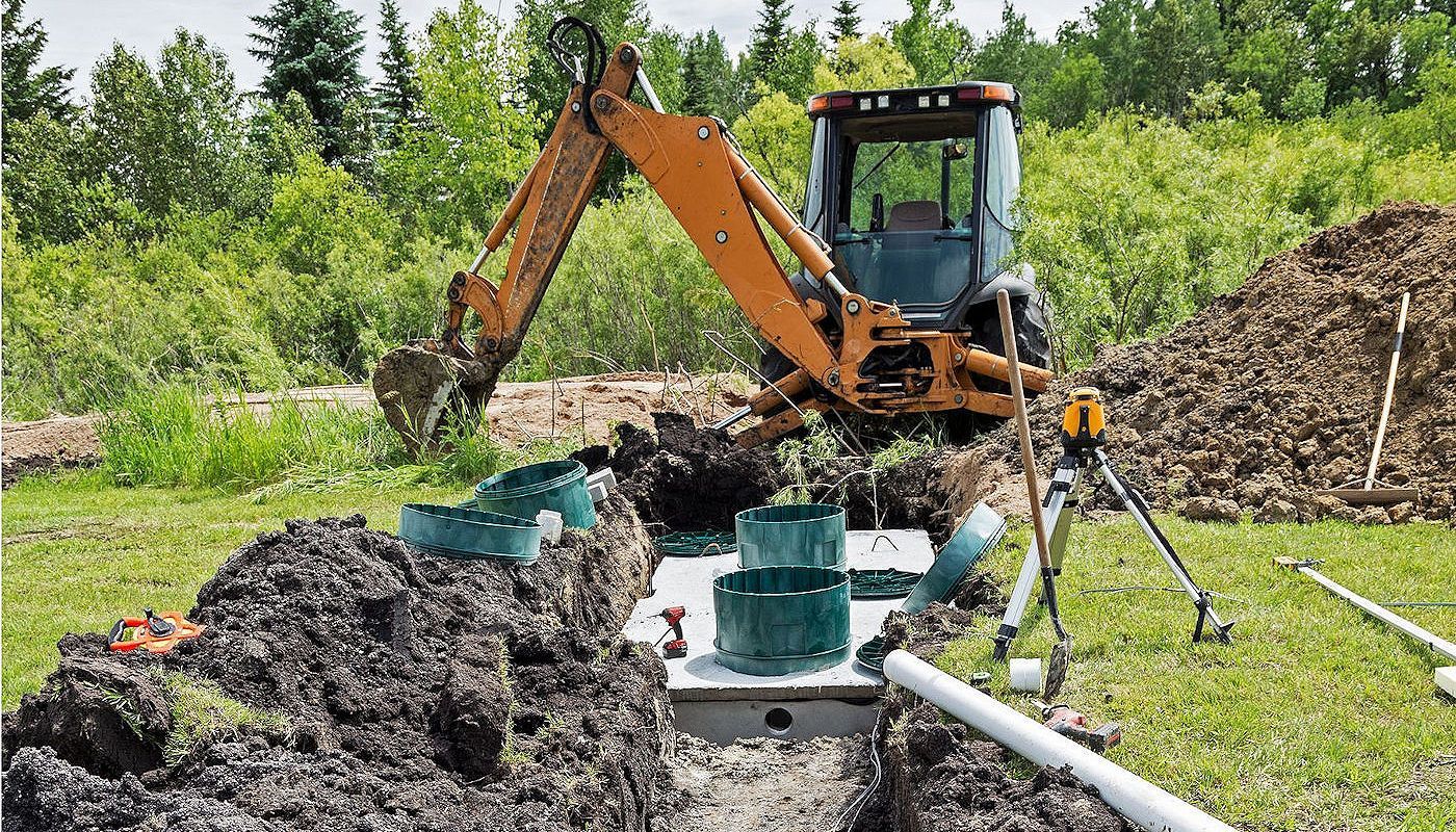 Excavator digging near a septic tank installation in a grassy field.