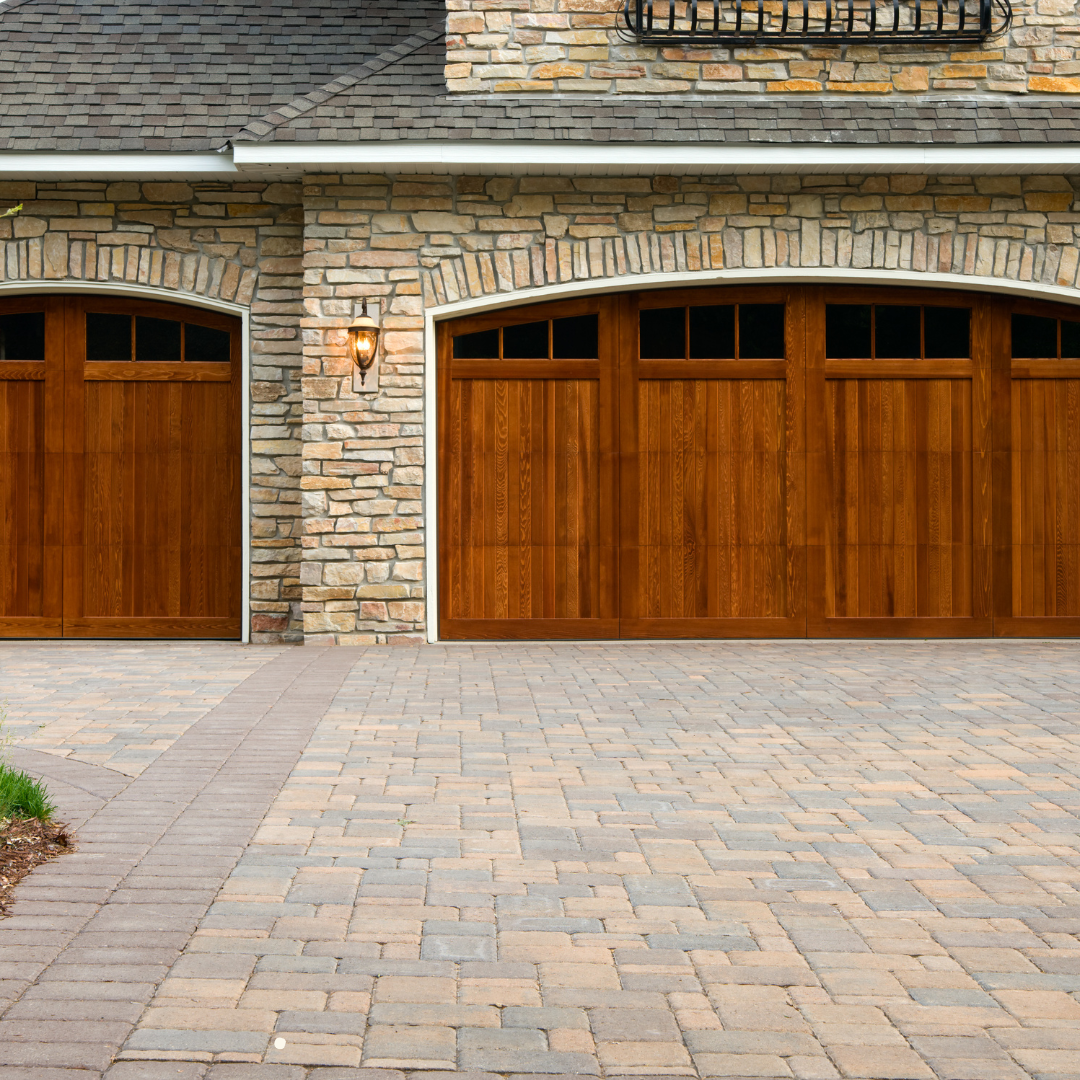 A stone building with wooden garage doors and a brick driveway
