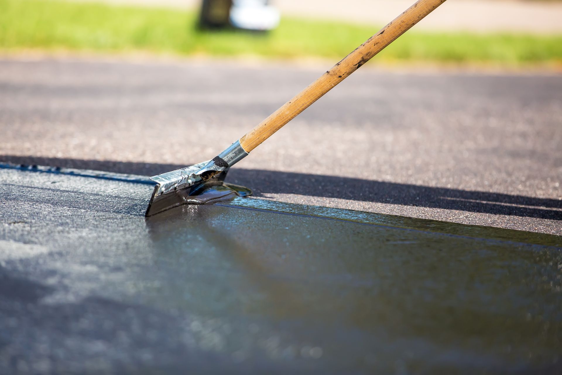 Worker performing driveway sealcoating on asphalt surface using a roller