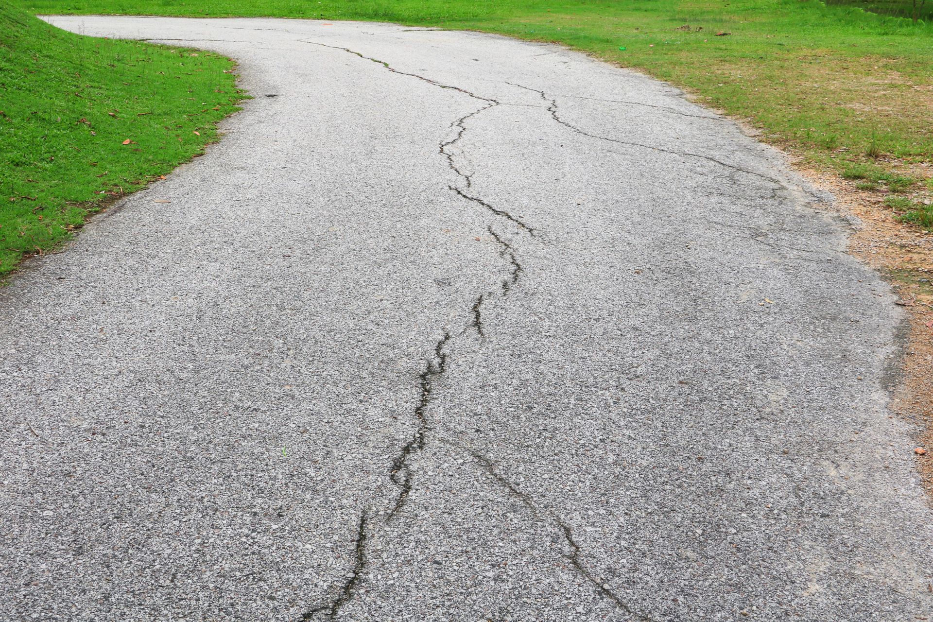 Cracked and worn asphalt driveway in need of repair and sealcoating offered by CM Ayres