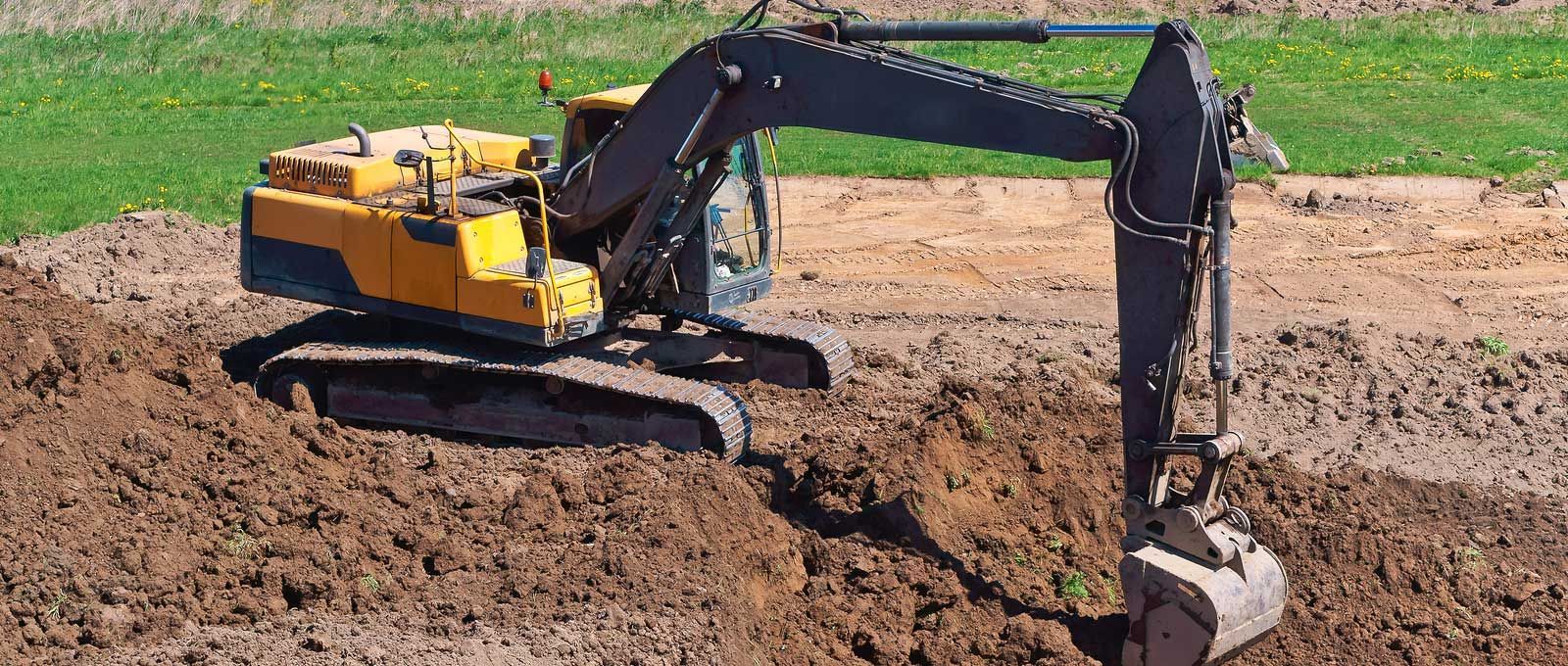 Yellow excavator digging in dirt, with green grass in the background.