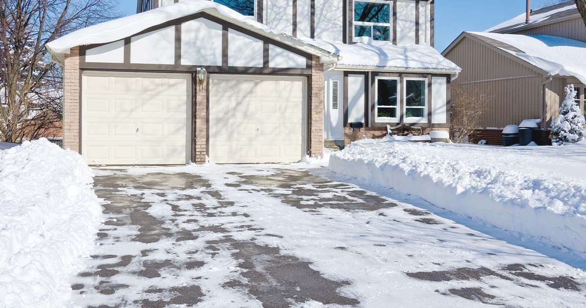 Snow-covered driveway leading to a two-car garage and house in winter.