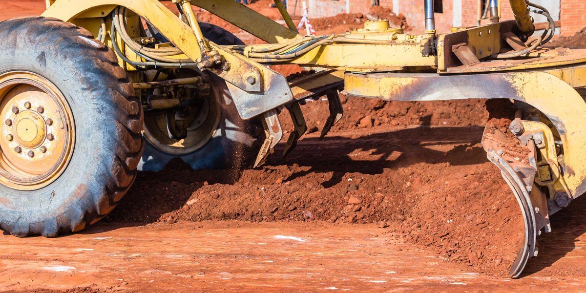 Yellow excavator digging dirt on a brown, dirt path under a blue sky.