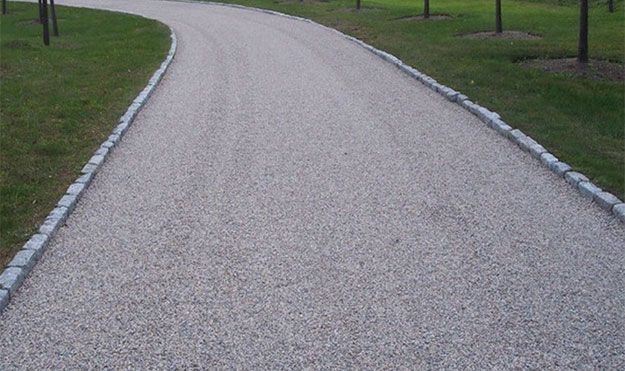 A gravel driveway going through a grassy area.