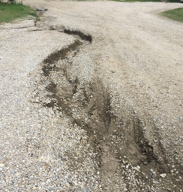 Gravel road eroded by water, forming a deep channel.