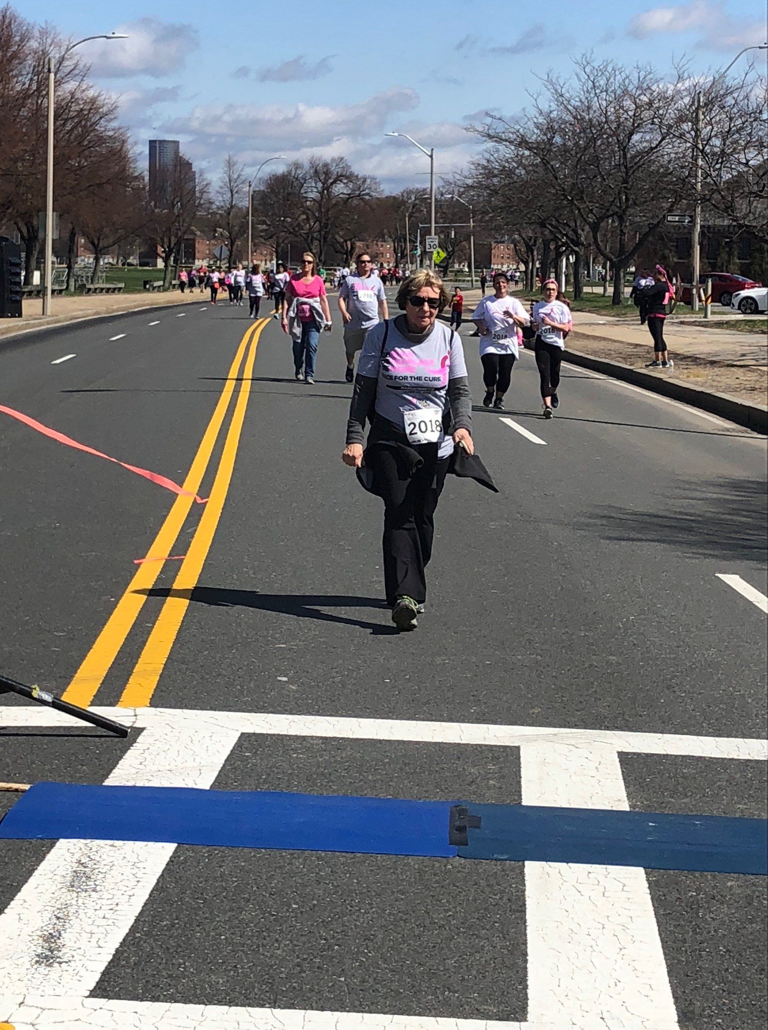 People walking and running a race on a city street; sunny day.