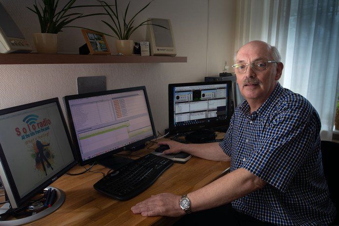 Een man zit aan een bureau en bedient computers, ogenschijnlijk uitzendend vanuit een thuisstudio.