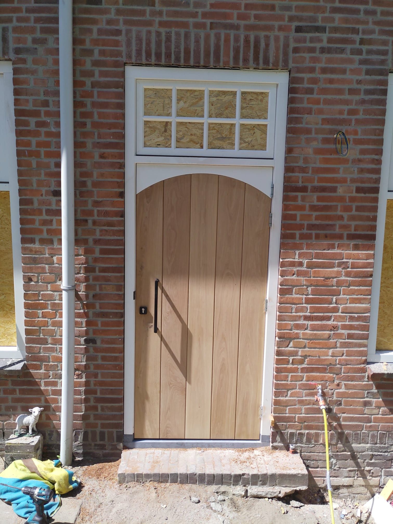 Voor een bakstenen gebouw staat een houten deur.