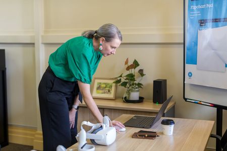 A woman is sitting at a desk with a laptop and talking on a cell phone.