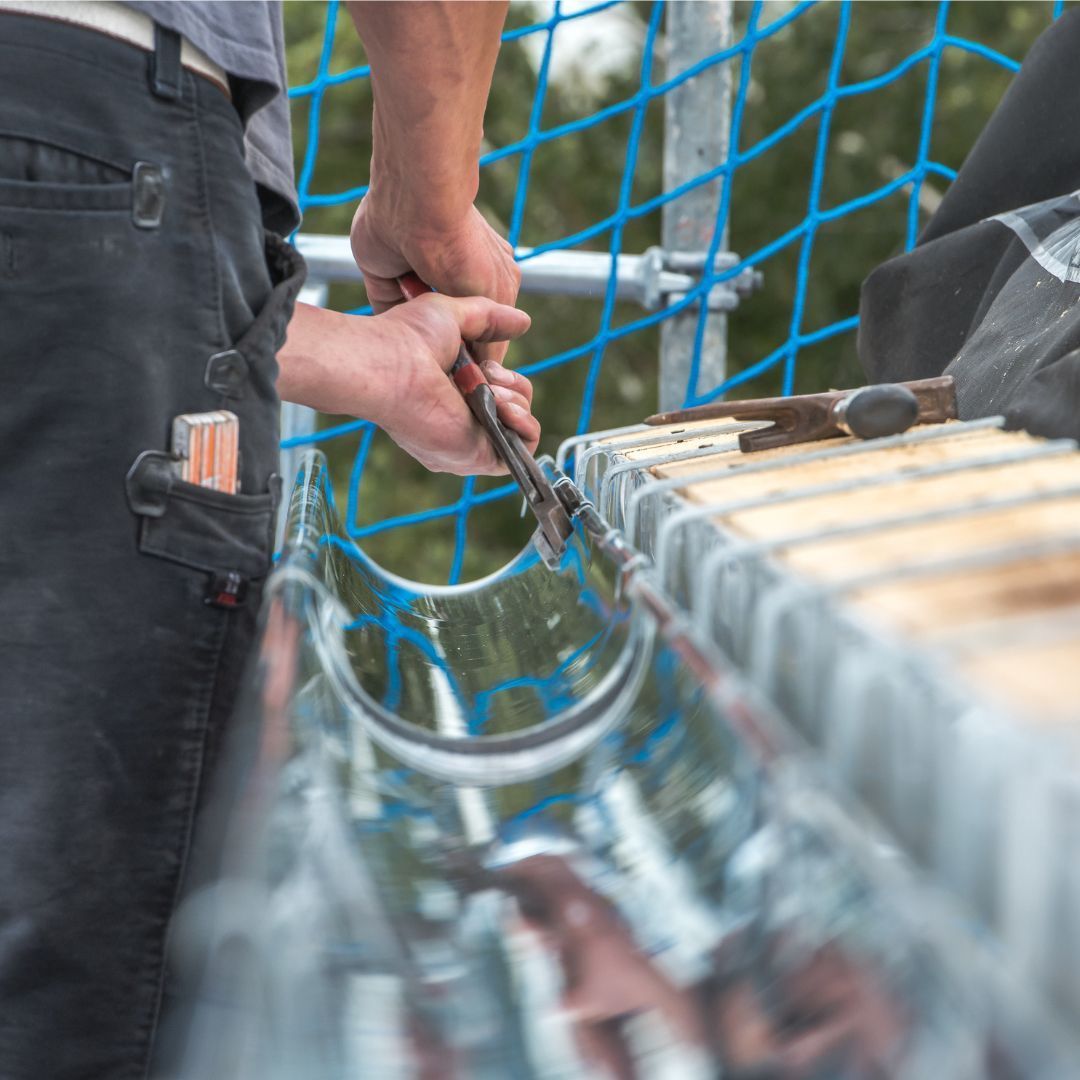 A man is working on a gutter with a pair of pliers.