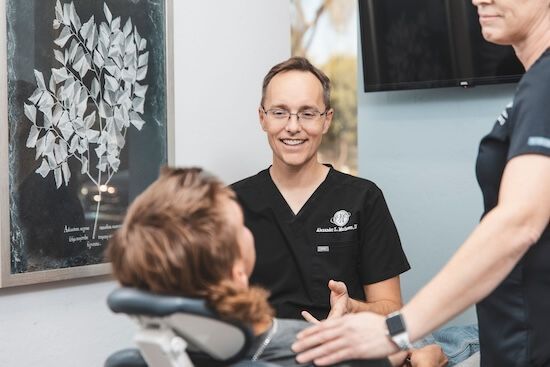 Two dentists are talking to a patient in a dental chair.