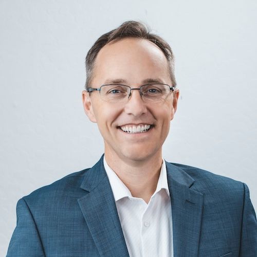 A man in a suit and glasses is smiling for the camera.