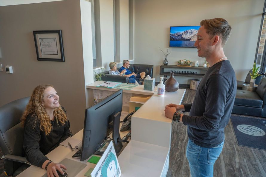 A man is talking to a woman at a reception desk in a dental office.