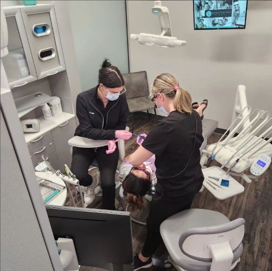 A woman in a dental chair is being examined by two female dentists