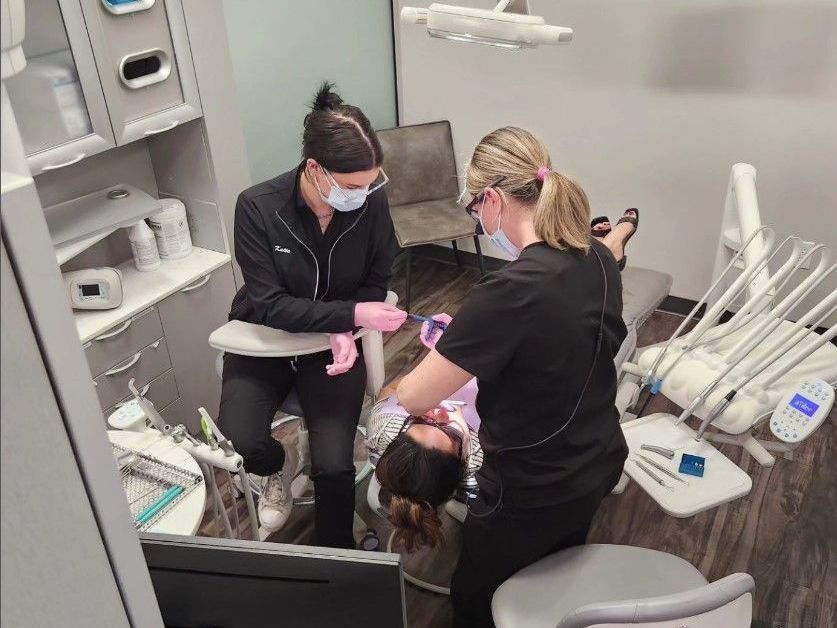 Two women are working on a patient in a dental office.