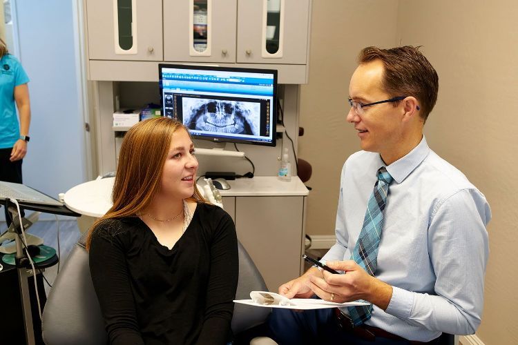A woman is sitting in a dental chair talking to a dentist.
