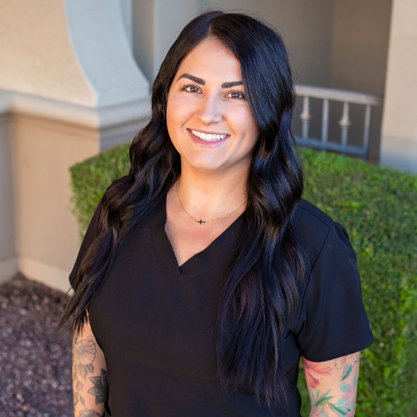 A woman in a black scrub top is smiling and standing in front of a building.